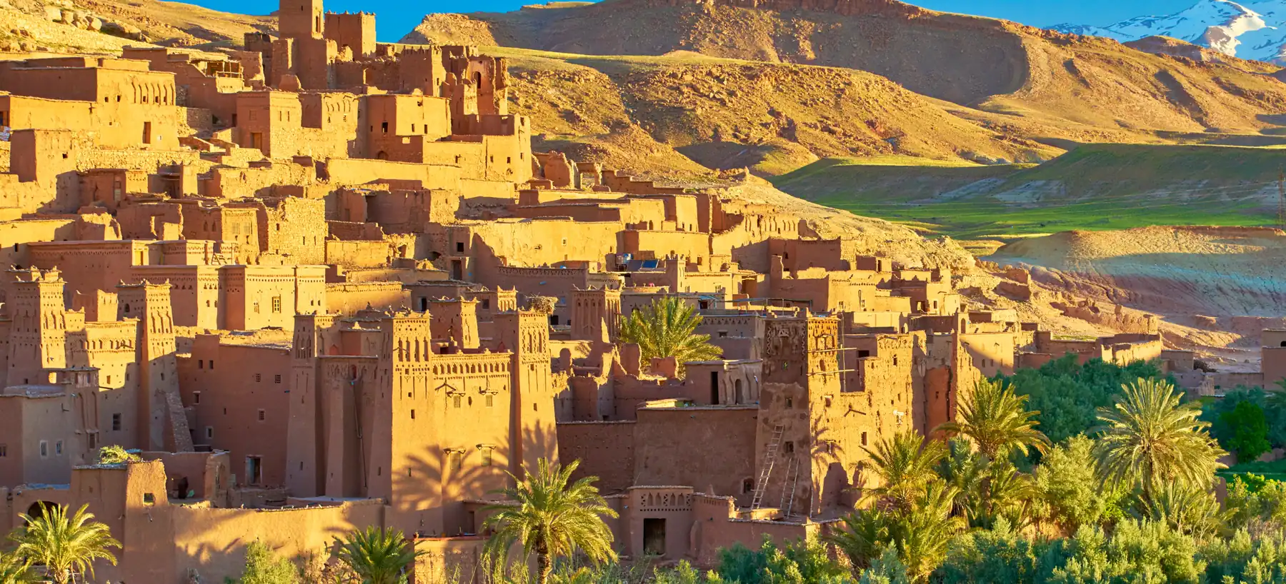 The earth-built kasbah of Aït Benhaddou near Ouarzazate in warm light, with palms below and hills behind