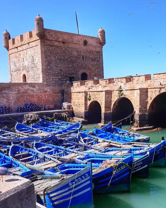Blue fishing boats in Essaouira harbour below the old sea fortress and its arches