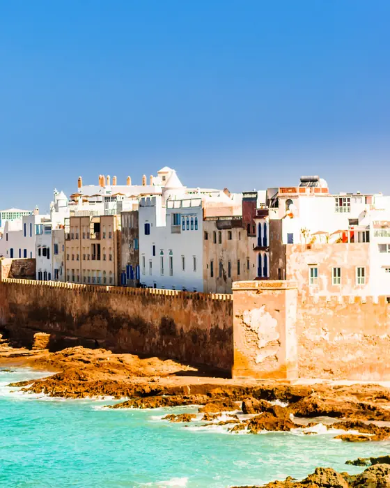 The ramparts and white houses of the old city of Essaouira above turquoise water and rocks