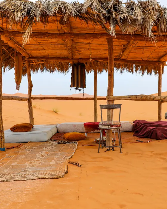 A palm-thatch shelter with rugs and cushions on the orange dunes near Merzouga
