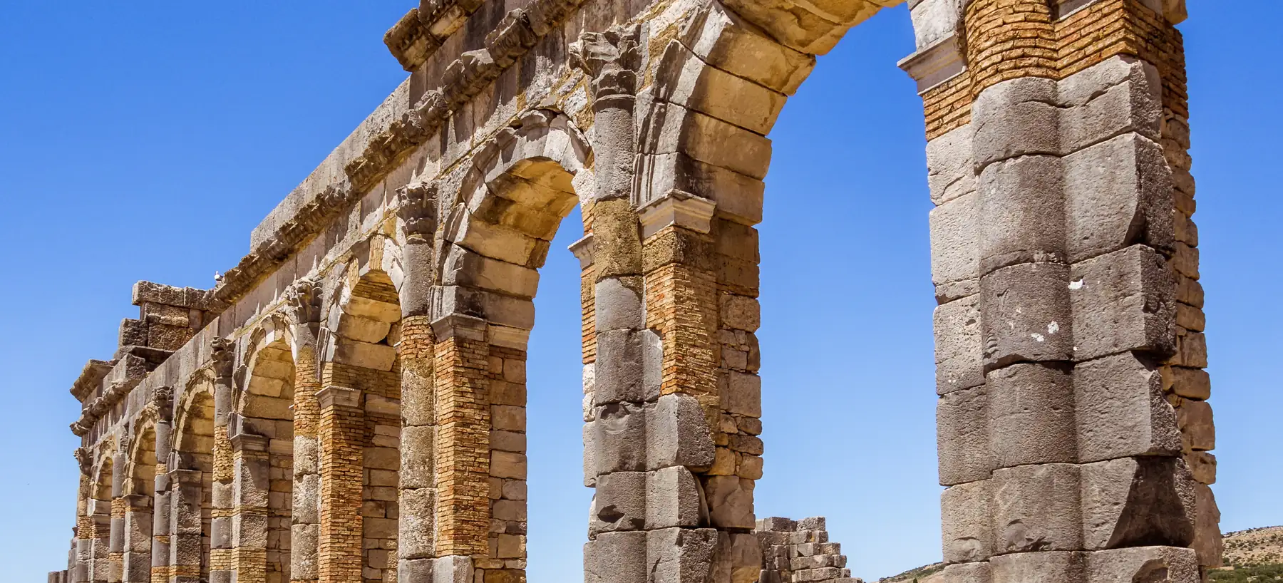 Roman arches and stone columns at Volubilis under a blue sky